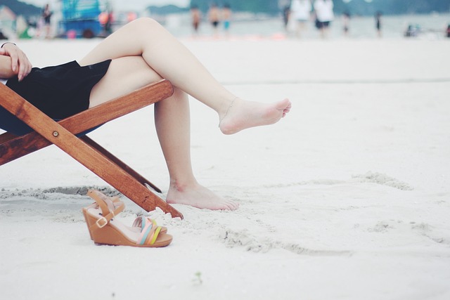 A person relaxing on a beach chair with bare legs, enjoying a sunny day on the sandy beach. Perfect example of free leisure activities in Dubai, such as visiting public beaches.